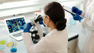 Hybrid life sciences training session with instructor and trainee in cleanroom gear engaging remote participants via video wall.